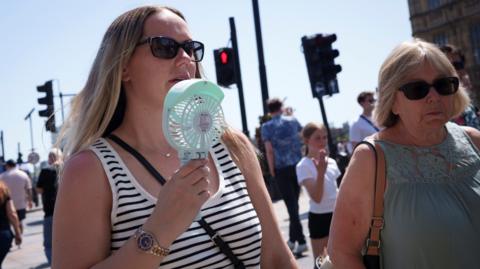 A woman cools herself with a handheld electric fan