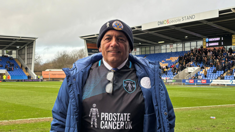 Dave Cossie at Shrewsbury Town's New Meadow stadium, with a blue jacket and woolly hat and a black prostate Cancer UK shirt