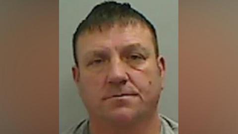 Mugshot of Pearce. He is white, clean shaven, of a stocky build and has short brown hair.