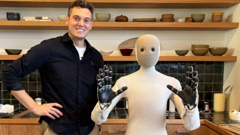 A smiling man pictured next to a domestic robot in a kitchen