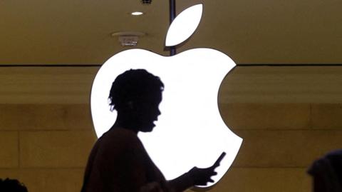 A person on their phone in front of the Apple logo