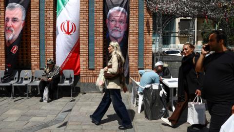 A woman walks past a banner with a picture of the late Iranian security chief Ali Larijani in Tehran Bazaar, Tehran.