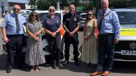 Debbie is pictured with members of the CFR team and a mayor and they are standing in front of two vehicles. Debbie is in a patterned sundress and Ellie is wearing a yellow dress. A male and female responder are wearing a navy uniform two other men, on the far left and right, are wearing a navy shirt and trousers. The man on the right is wearing mayoral chains over his shirt Tim Bridgland-Taylor (Hereford Freemasons), Debbie Roscoe(Arrive Alive Founder), Fran Thomas (community first responder), Daryl Szebesta (community first responder) Ellie Roscoe (Debbie’s daughter), Stuart Jones (Hereford Freemasons)