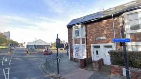 The junction of Warwick Street. City Stadium is to the left. A Warwick Street sign is on a house which has been boarded up.