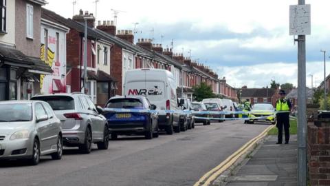 The cordon in St Paul's Street in Swindon. It is a residential street, with rows of terraced houses and parking to the left hand side. There are double yellow lines on the right of the carriageway.