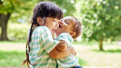 Older sister embraces younger brother, wearing matching green stripey t-shirts.