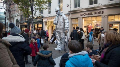 Silver painted living statue street performer sits totally still as if floating in mid air, and delighting passers by and tourists in Covent Garden, London