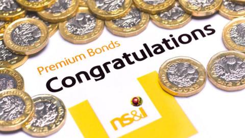 A pile of silver and gold coloured one pound coins arranged around words which read Premium Bonds, congratulations, NS&I