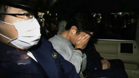 Takahiro Shiraishi holds his face in his hands in the back of a vehicle