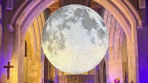 A 3D dimensional suspended moon installation hangs in a church.