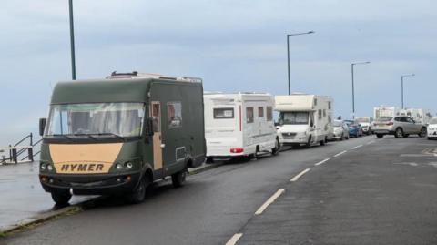 A row of motorhomes and cars parked on a Saltburn seafront on a grey day.
