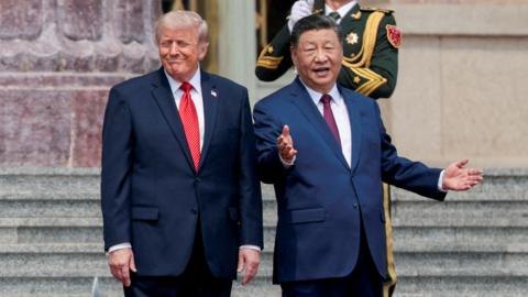 Xi stands with his hands outstretched as Trump smiles on the stairs. A soldier can be seen standing behind them