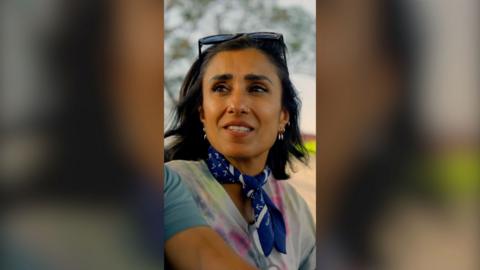 A woman with short dark hair, outside looks to someone out of shot, to her right.