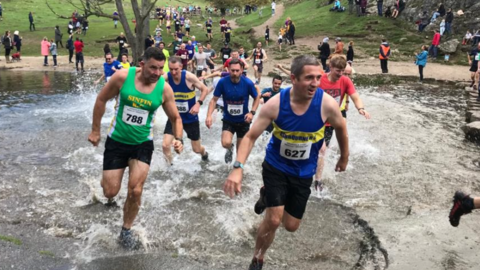 Multiple people running across the foot-high River Dove in Derbyshire for the annual Dovedale Dash event 