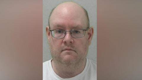 Mugshot of Michael Grey. He is bald with faint stubble and glasses.