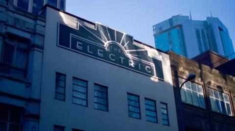 A white multi-storey building with a sign in Art Deco style that says "The Electric"