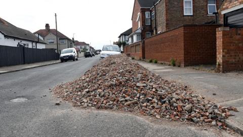 A large pile of bricks dumped by the curb on Sherburn Street in Cleethorpes. Houses and cars are seen in the background.