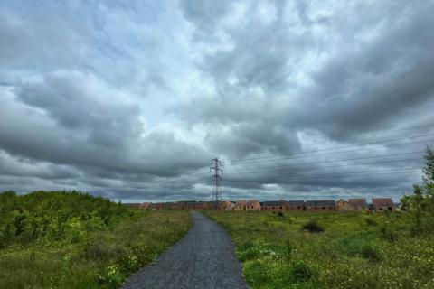 A gravel path leads through wild grass toward houses under dark, stormy clouds in Wallsend, North Tyneside