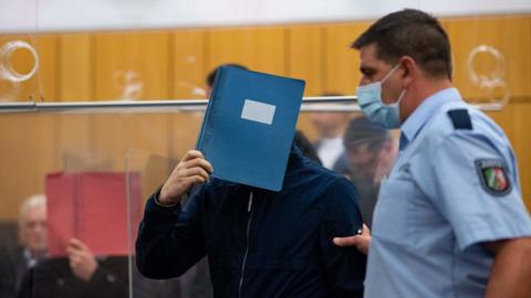 The main defendant hides his face behind a folder in court