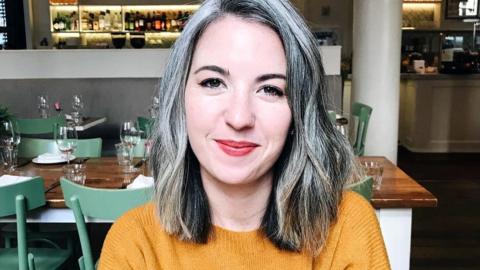 Kate, who has a grey curly bob, is pictured sitting in a restaurant