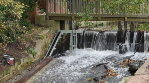 A metal chute next to a weir with a footbridge running over it