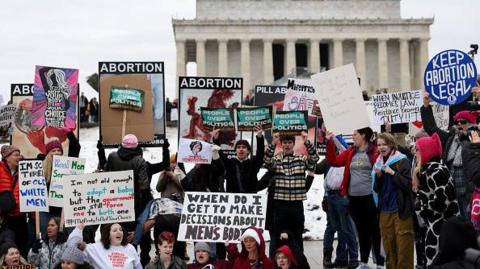 A crowd holds signs outside the Lincoln memorial 