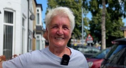 Eileen Harland is pictured on her street smiling into the camera, she has short blonde hair and is wearing a grey t-shirt