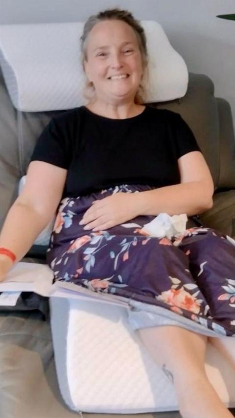 Woman sits on sofa smiling.