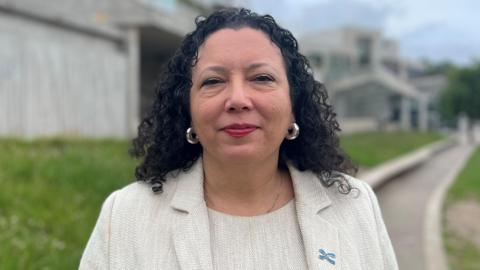 A woman with black hair wearing a cream coloured matching suit jacket and top 