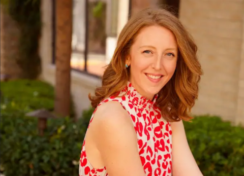 A red-haired woman in a red and white dress smiling and pictured outside