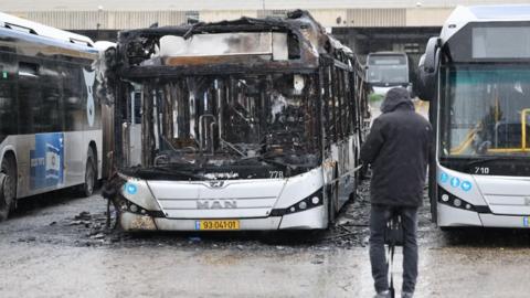 Man looks at charred remains of bus (21/02/25)