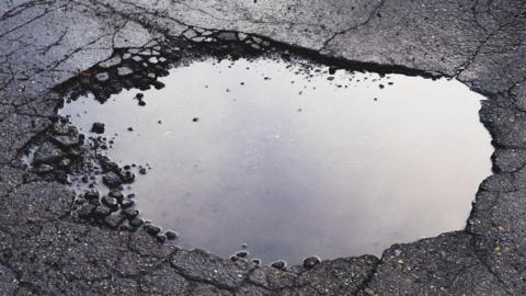 A close-up of a pothole on a Tarmac road, with water in it.