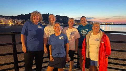 Six women are all smiles at the water's edge before heading off on a cross Channel swim