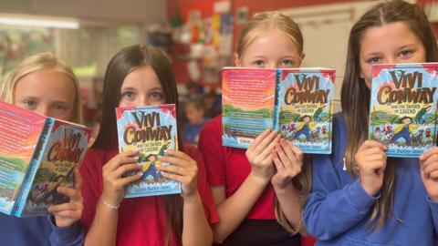 Four girls holding books in front of their faces