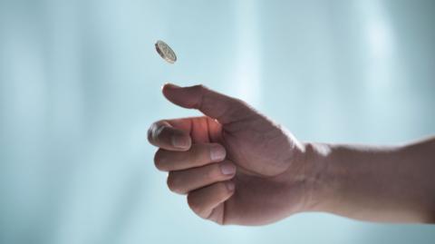 A picture of a hand flipping a one pound coin.