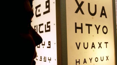 A silhouette of a person reading an eye test chart