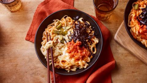 A top-down view of a bowl with kimchi udon noodles. Next to it is a glass of water.