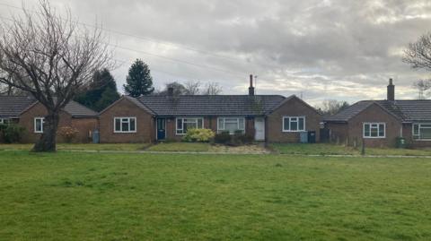 A green space with a bungalow in the background.
