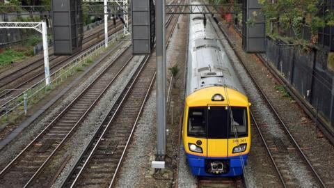 An Overground train with a yellow front hub and blue trim beneath taken from above with tracks either side.