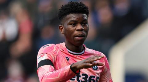 Stoke City's Sol Sidibe is wearing the club's pink away kit and is stretching out his right hand during a stoppage in play