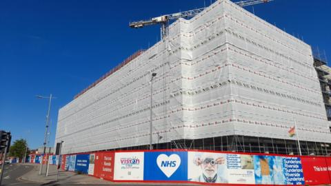 The building that will host Sunderland’s new eye hospital is covered in protective grey sheeting. NHS boards are all around the lower floor of the site. A crane is visible above the building.
