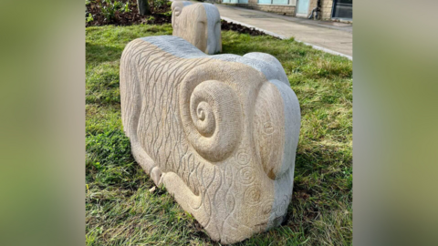 A stone sheep. It is a cuboid shape with rounded edges. It has curled horns on the side.