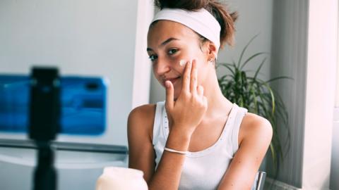 Teenage girl watching a skin care tutorial and applying a face mask or organic face cream in home 