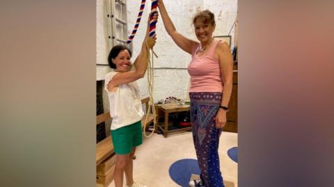 Two woman hold a rope connected to a church bell.