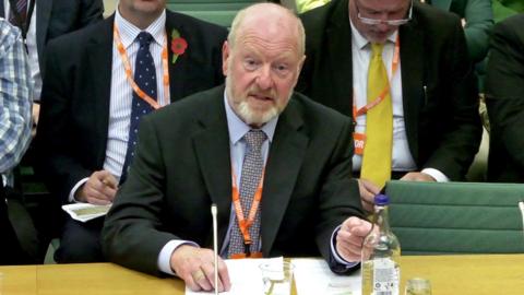 Sir Alan Bates giving evidence to MPs, sitting at a table with paperwork and a microphone in front of him