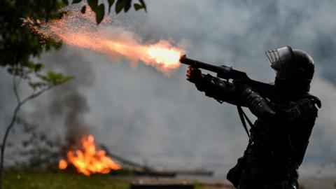 A riot police officer fires tear gas at demonstrators during clashes following a protest against a tax reform bill in Cali, Colombia, 30 April