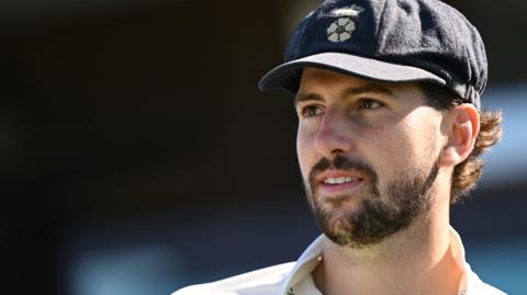 Ben Aitchison looks on wearing a blue Derbyshire cap