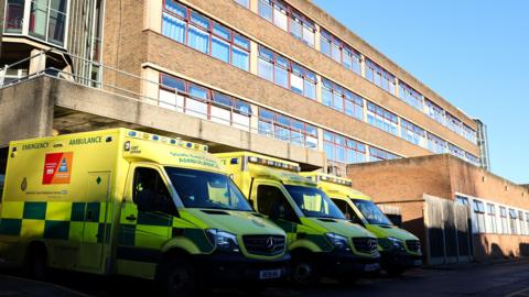 Green and yellow ambulances parked outside the red brick Royal Surrey Hospital.