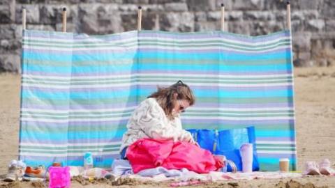 A woman sitting on the beach, with a bright pink jacket on her lap