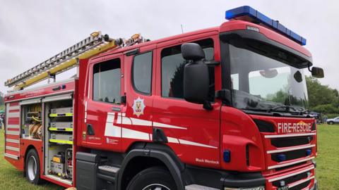 The side of a red fire engine parked on grass